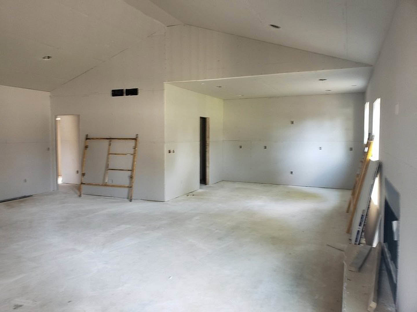 White-walled room with light flooring, multiple ladders leaning against the wall, and a door partially visible in the background