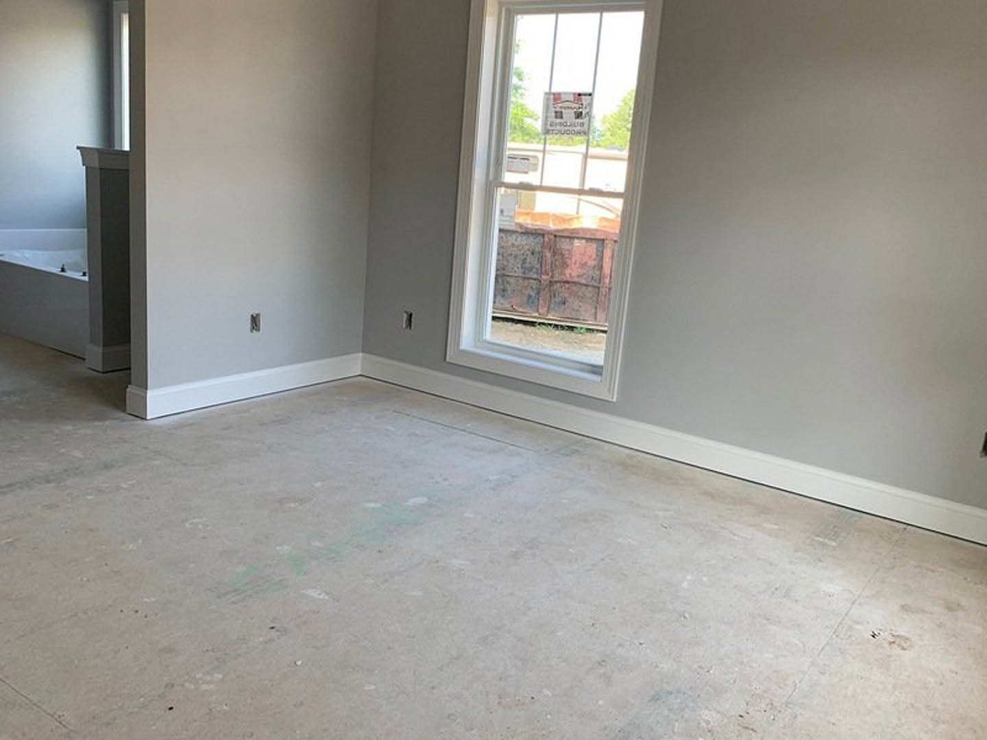 Sunlit room featuring a large window, smooth concrete floor, plaster walls, and a structural pillar near the corner.