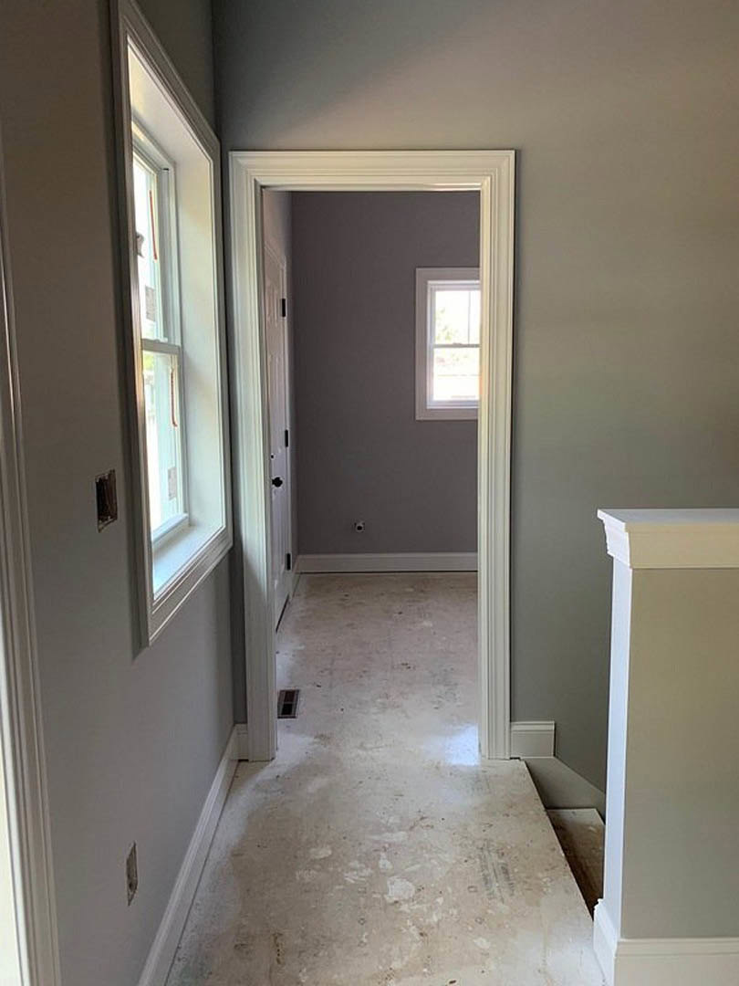 Hallway with white plaster walls, open door, dirty floor, and window letting in natural light