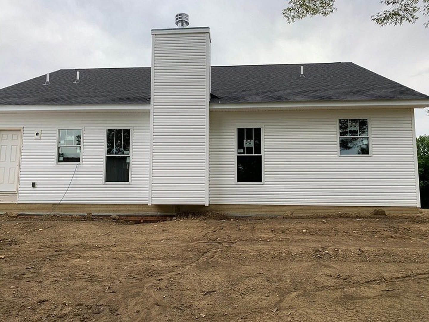 White cottage-style home with brick chimney, black-framed windows, white siding, and a wooden accent wall on dirt landscaping under a clear sky.