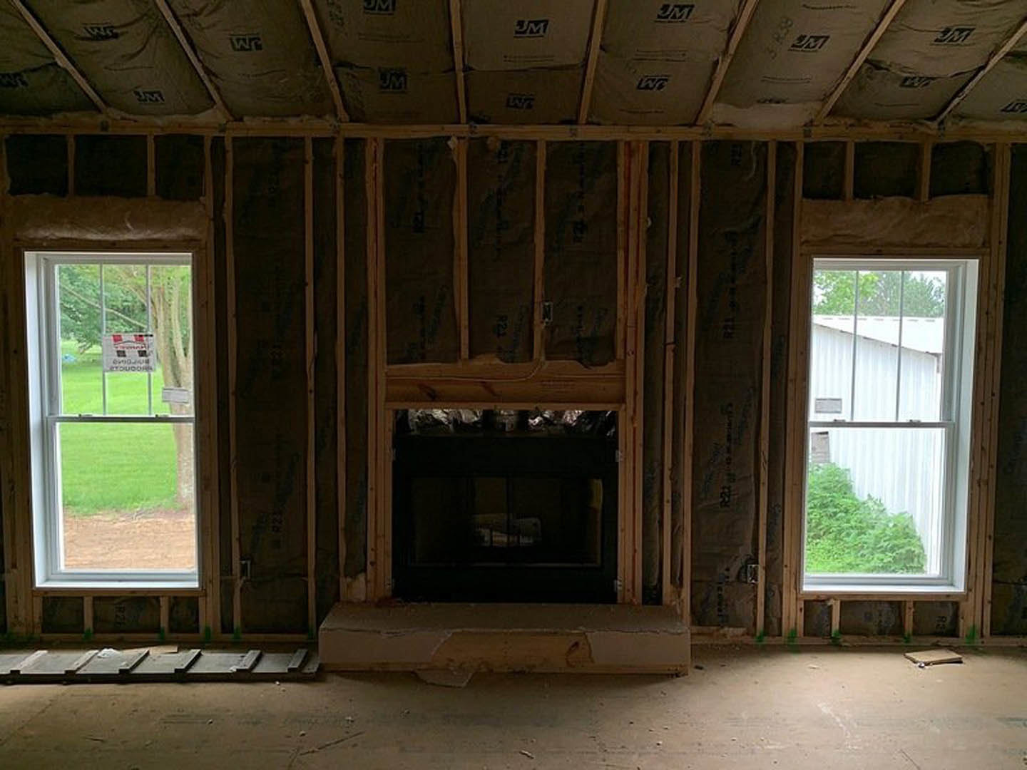 Living room with stone fireplace, large windows, white walls, hardwood floor, and potted green plant