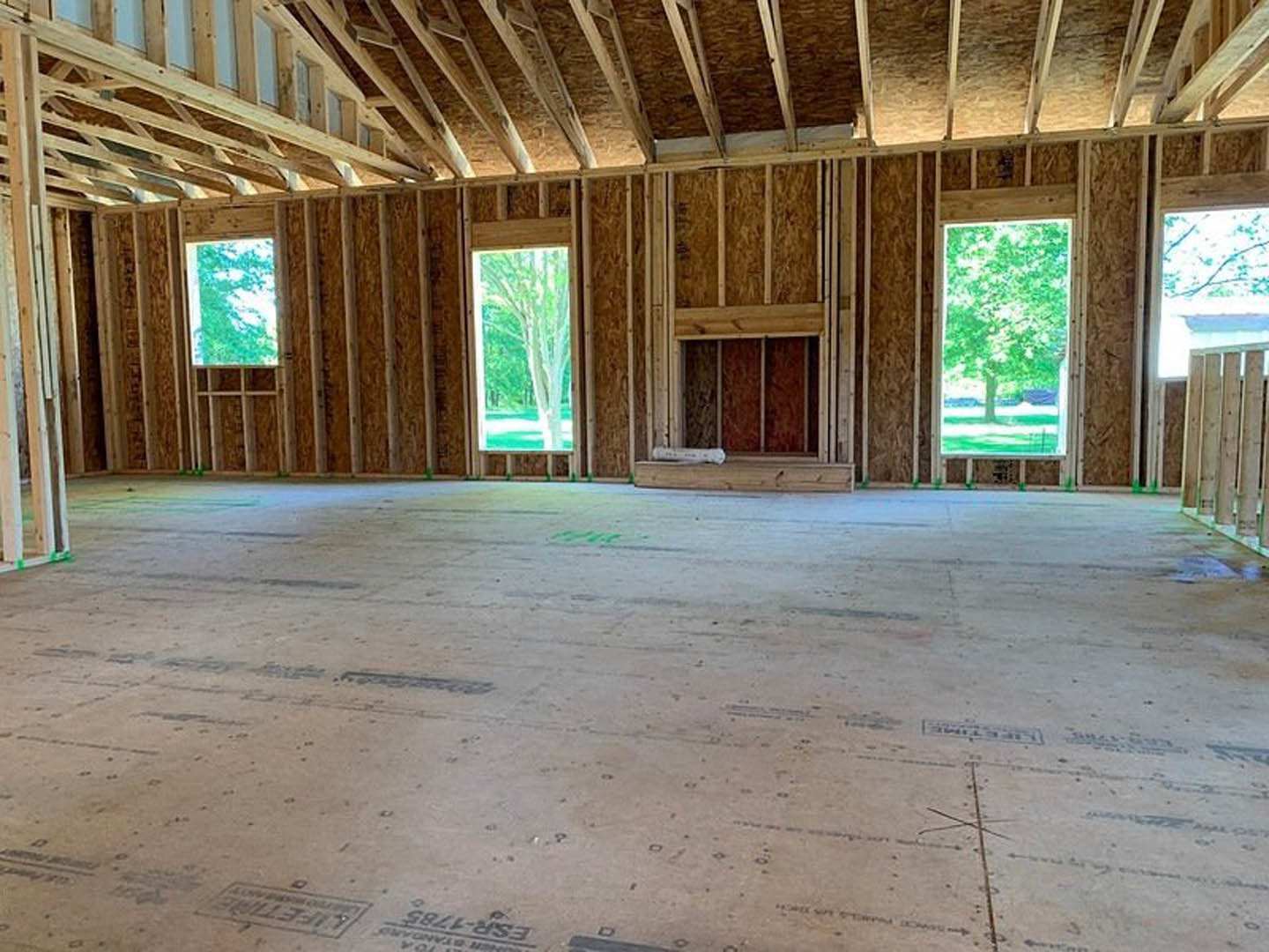 Living room with exposed wood ceiling beams, wide plank wooden floor, large windows framing leafy trees outside
