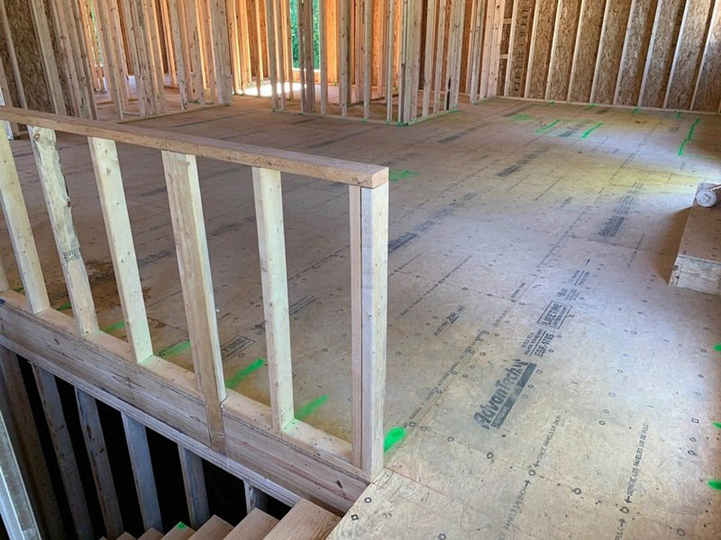 Exposed wooden framing and floor planks with partially installed handrails and balusters inside a house under construction