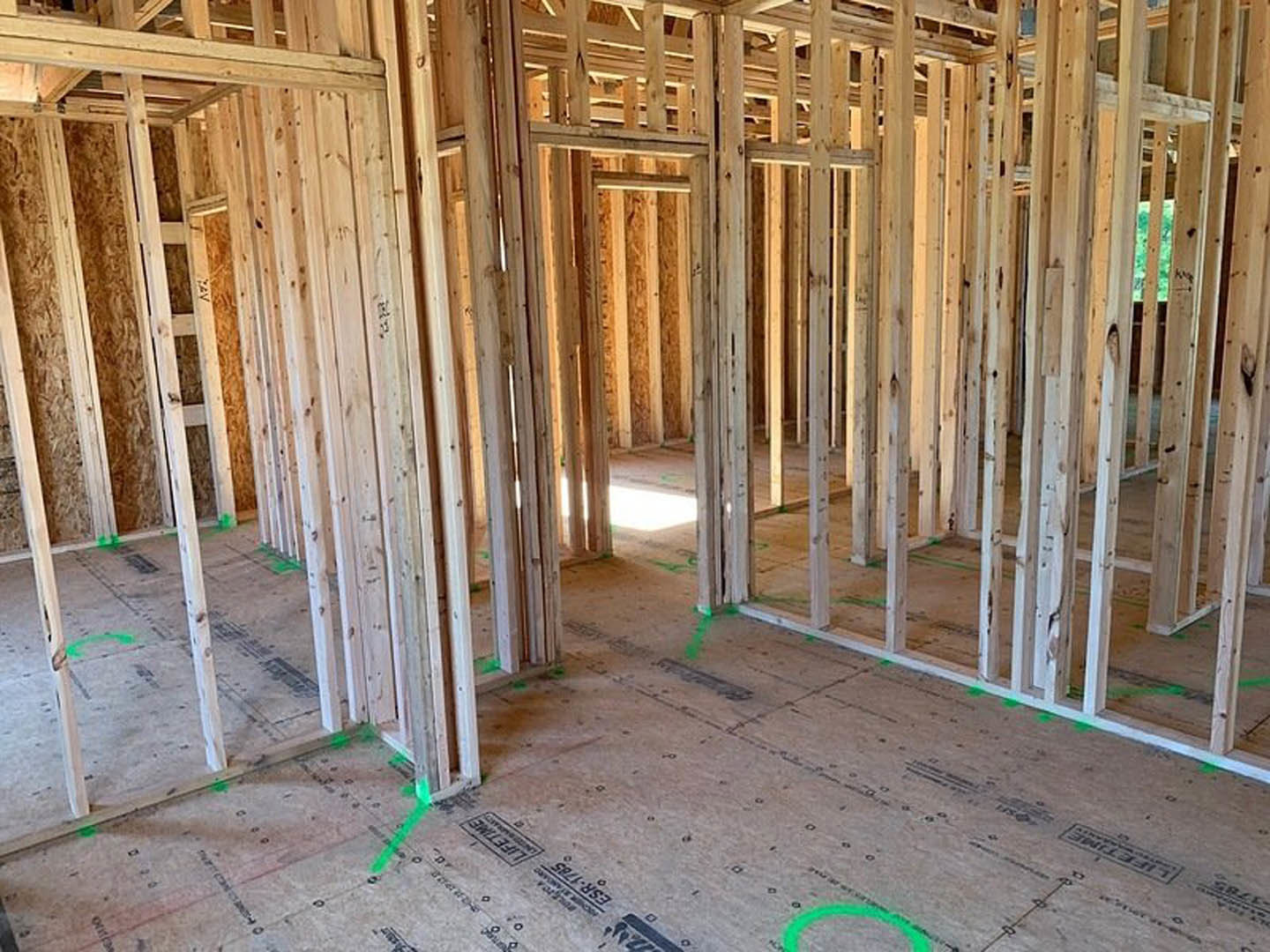 Wood-framed room with exposed beams, green painted line on grey subfloor, unfinished interior construction