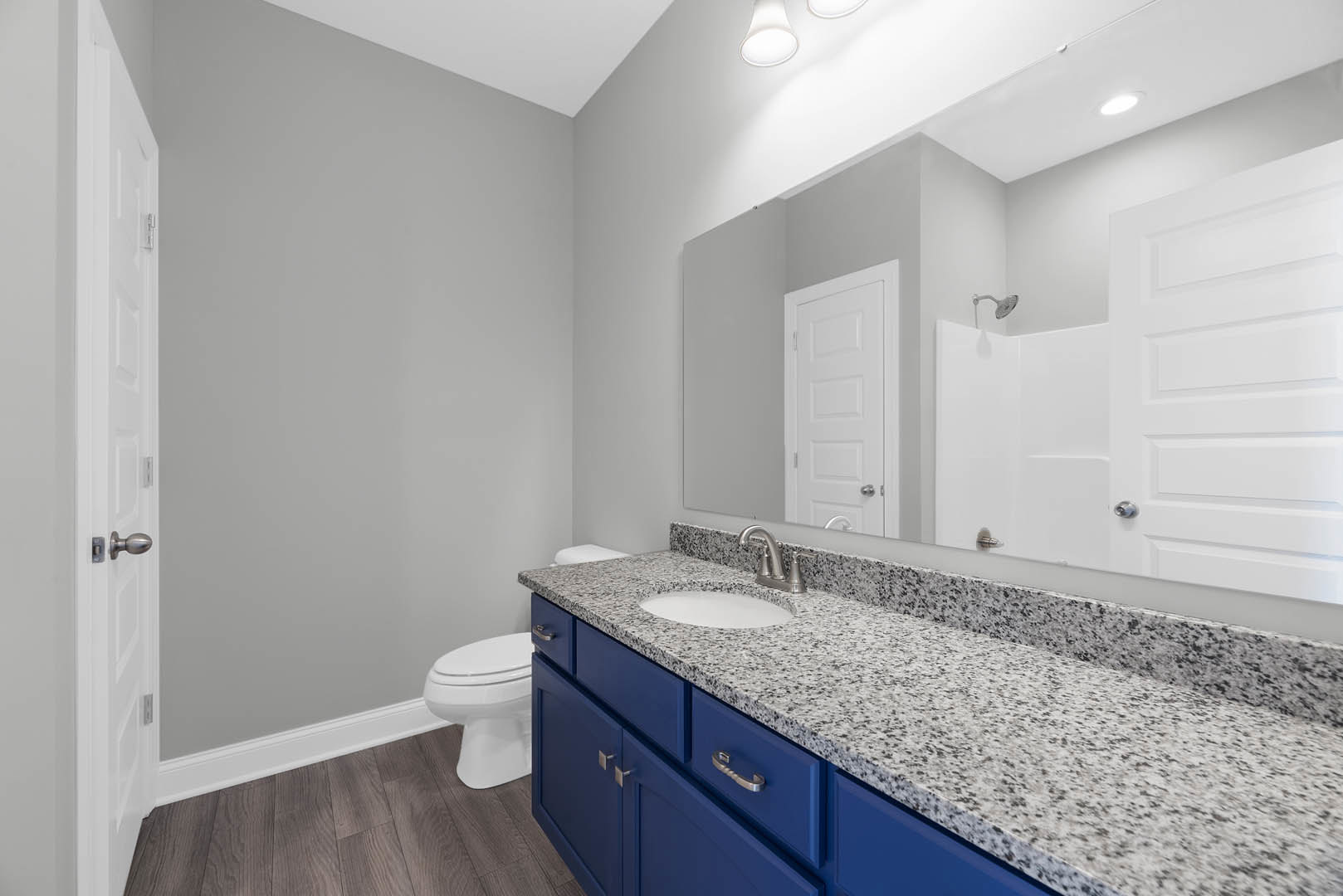 Bathroom with marble countertop, blue shaker cabinets, white undermount sink, silver faucet, and white paneled door with silver handles