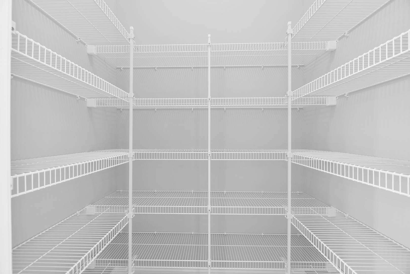 White wire shelving unit mounted on a wall in a room with a white background, featuring symmetrical metal shelves.