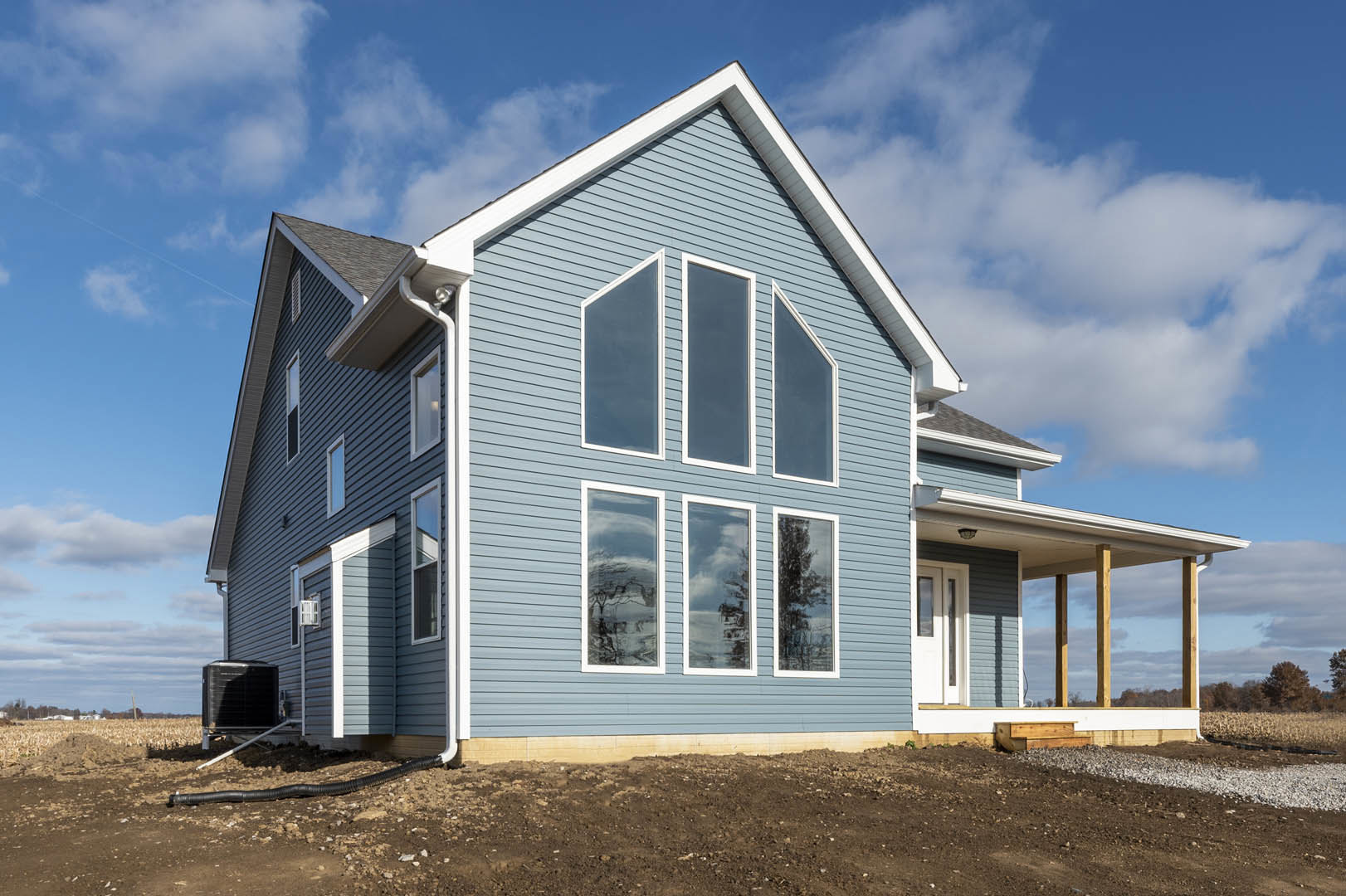 Blue siding with crisp white trim, large windows reflecting trees and clouds, under clear sky