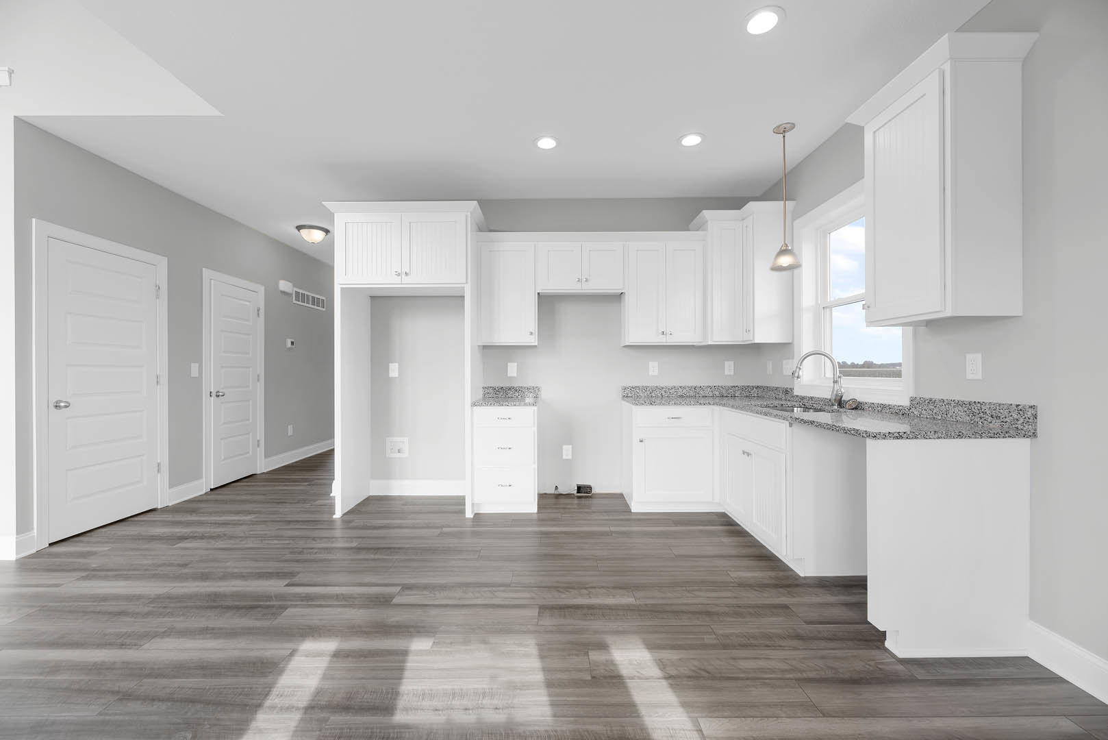 White kitchen cabinets with silver handles, granite countertops, stainless steel faucet, wood flooring, white walls, and a white door with a silver handle