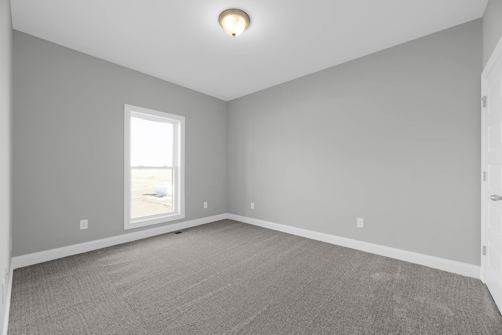 Carpeted room with white walls, large window overlooking grassy field, ceiling light fixture, small white object on floor near window