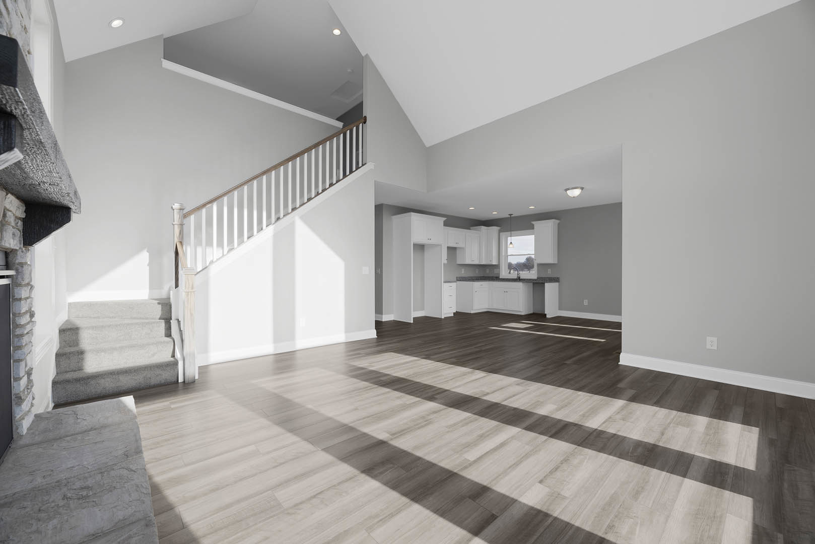 Spacious interior featuring white walls, wood flooring, and a central staircase with white risers and wooden railing; natural light casts shadows across the floor.