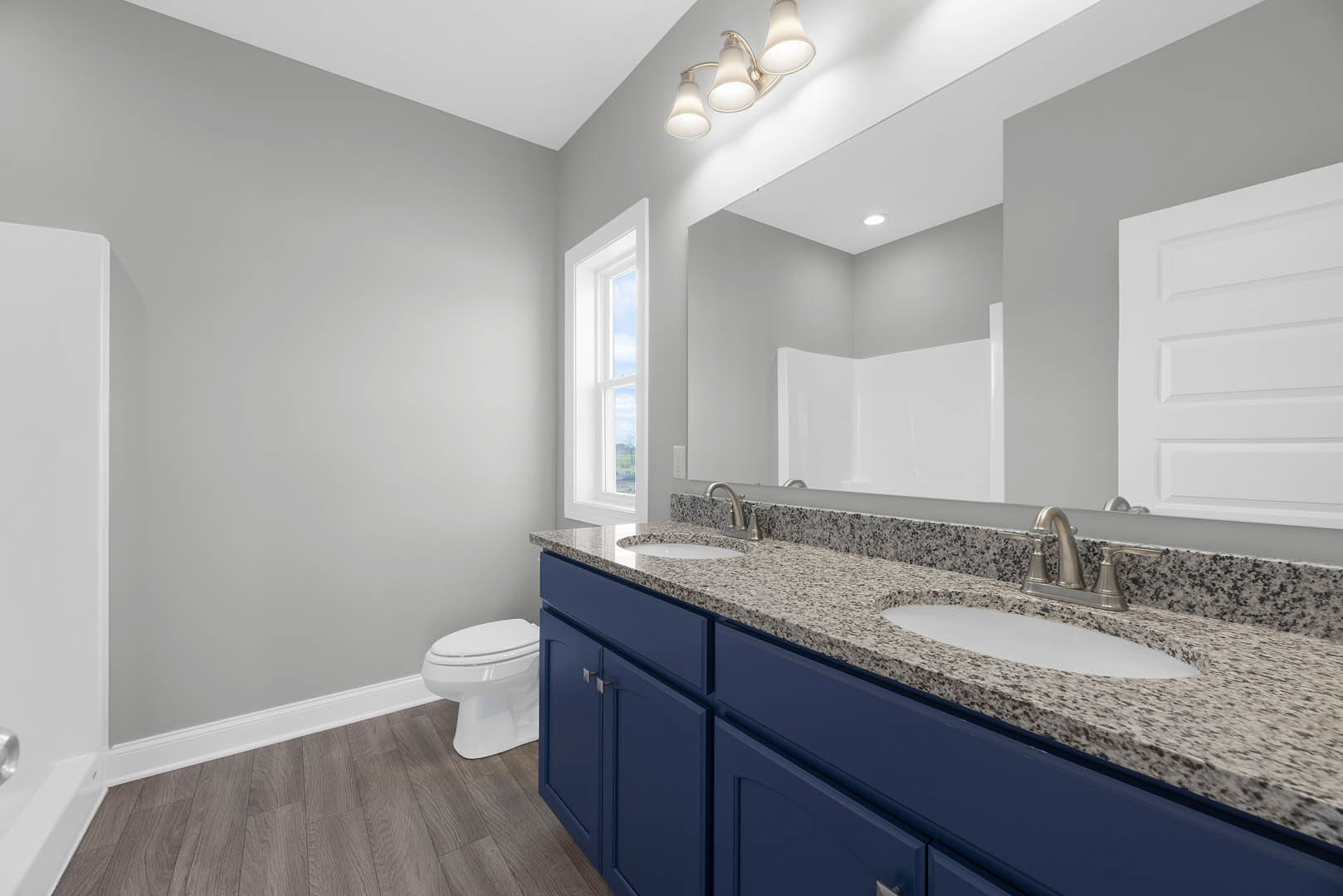 Bathroom with blue shaker cabinets, granite countertop, rectangular undermount sink, wall-mounted mirror, chrome faucet, white toilet, and tile flooring.
