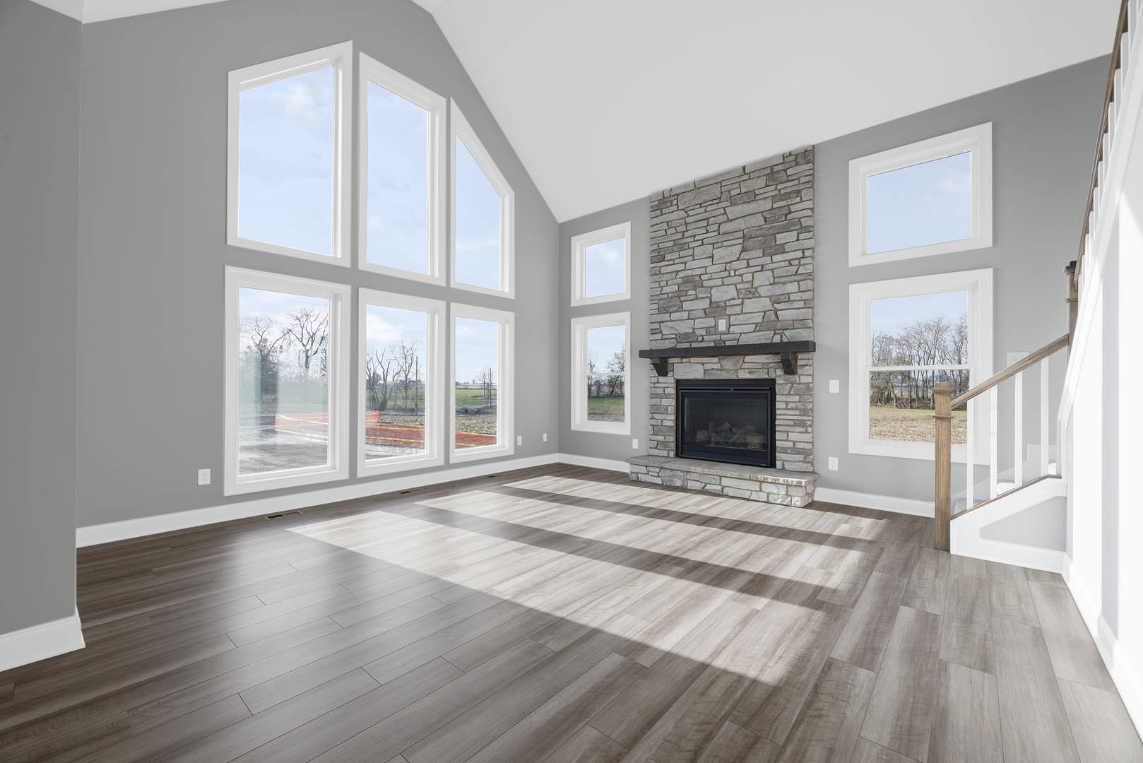 Spacious living area featuring wood flooring, a glass-door fireplace set in a white wall, and expansive windows framing a blue sky.