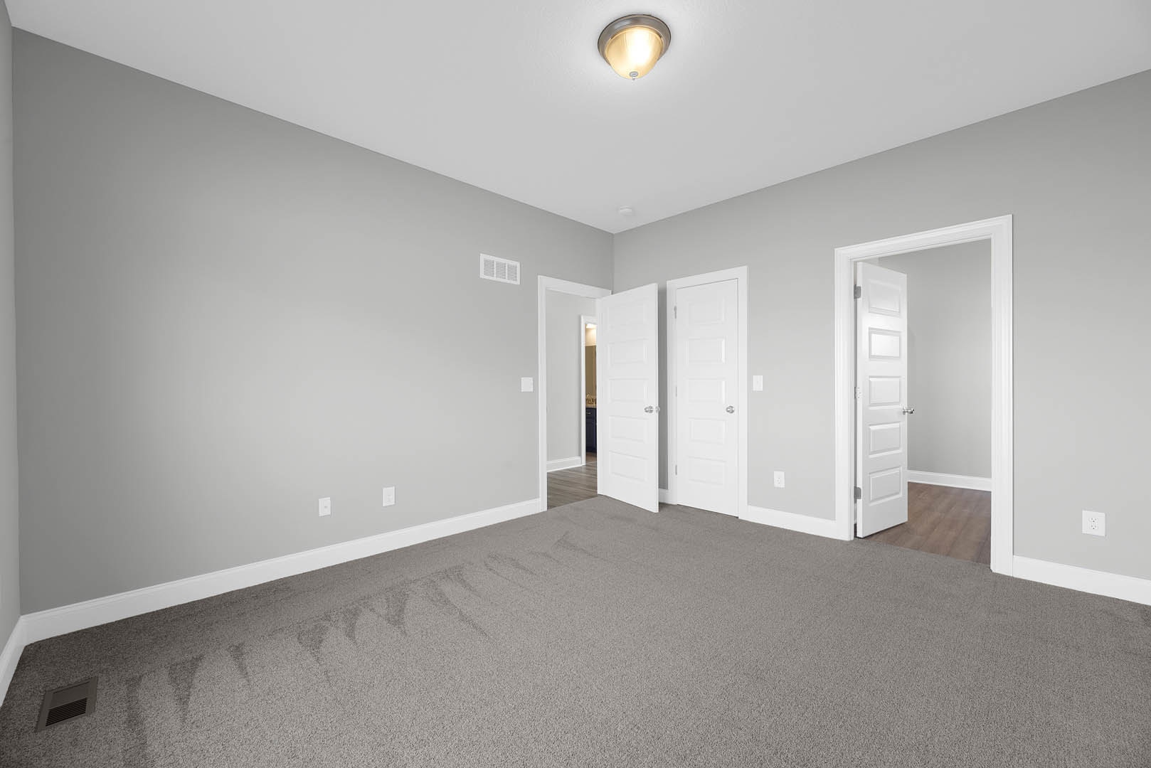 Carpeted room with white walls, multiple white doors featuring silver handles, ceiling-mounted light fixture, and visible bathroom door.