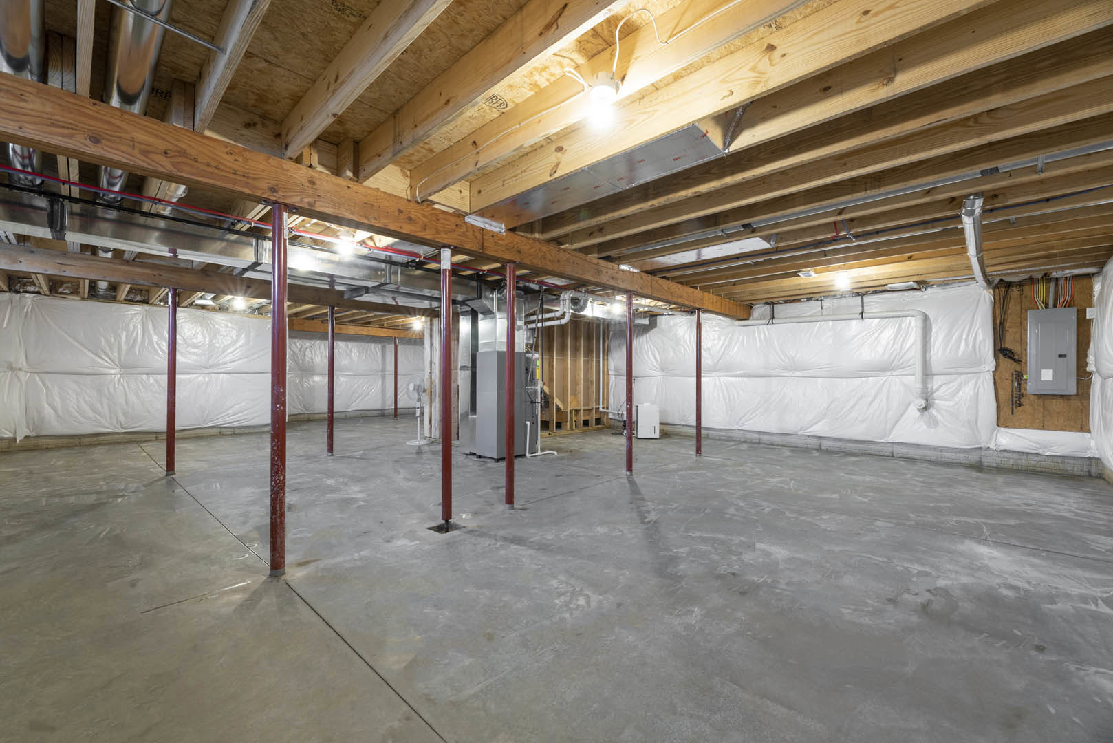 Wooden ceiling with exposed beams, white walls, white door featuring a black handle, concrete floor with red support poles, white plastic wall covering, ceiling-mounted light