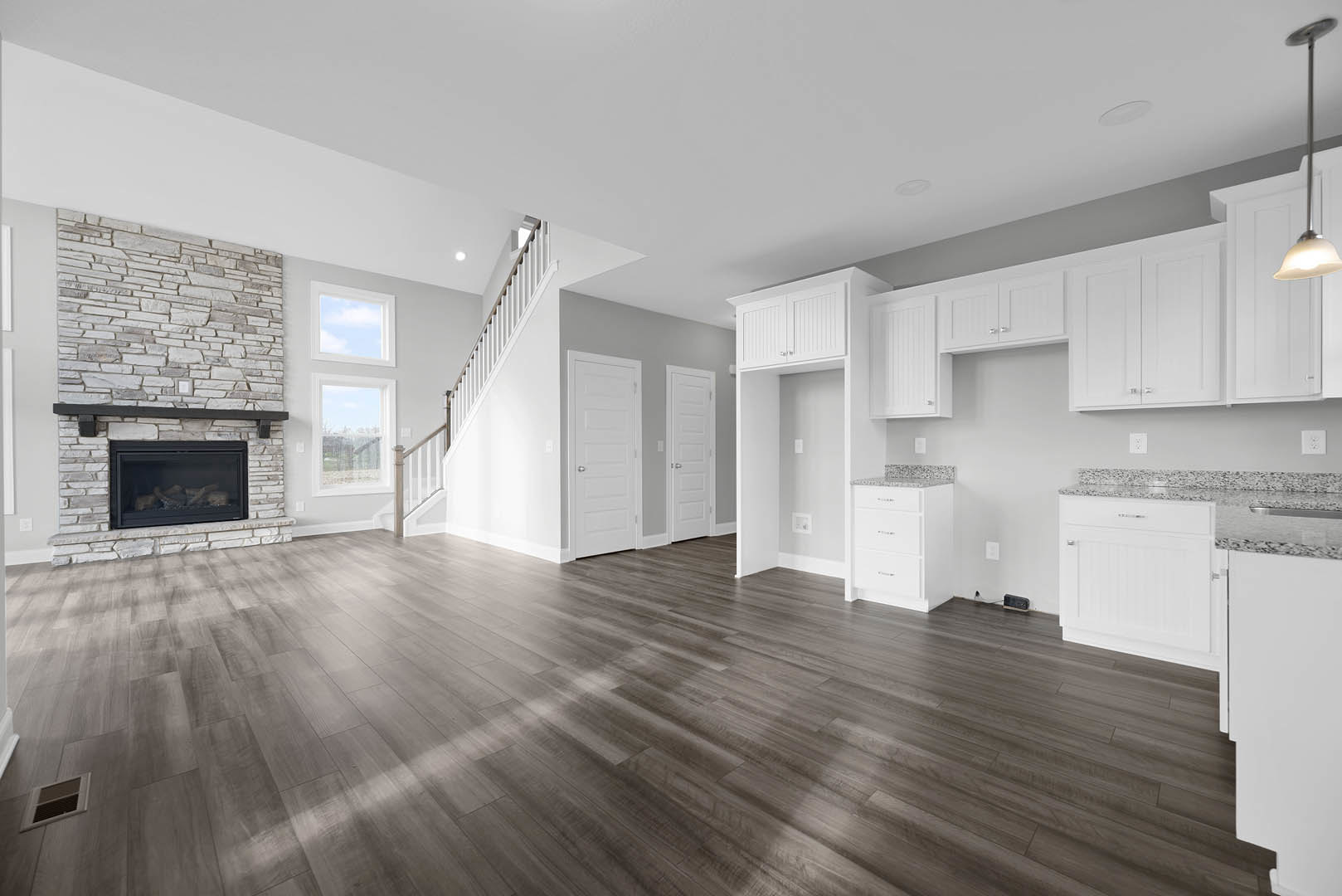 Spacious room with wood flooring, white doors, and a fireplace containing stacked logs; silver door knob and wall vent visible