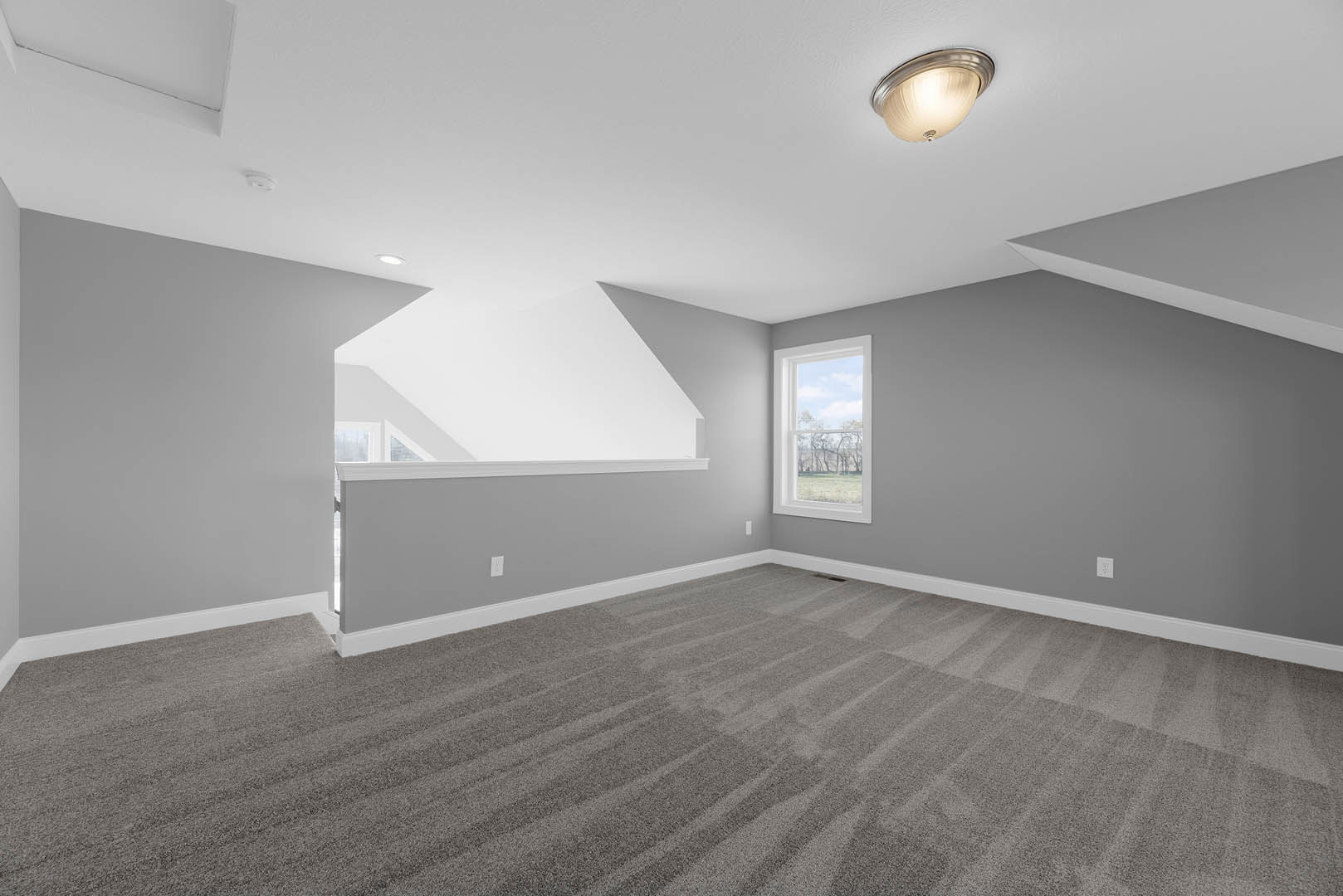 White ceiling with recessed light fixture, blue skylight, grey carpet flooring, large window overlooking green lawn, pale walls.