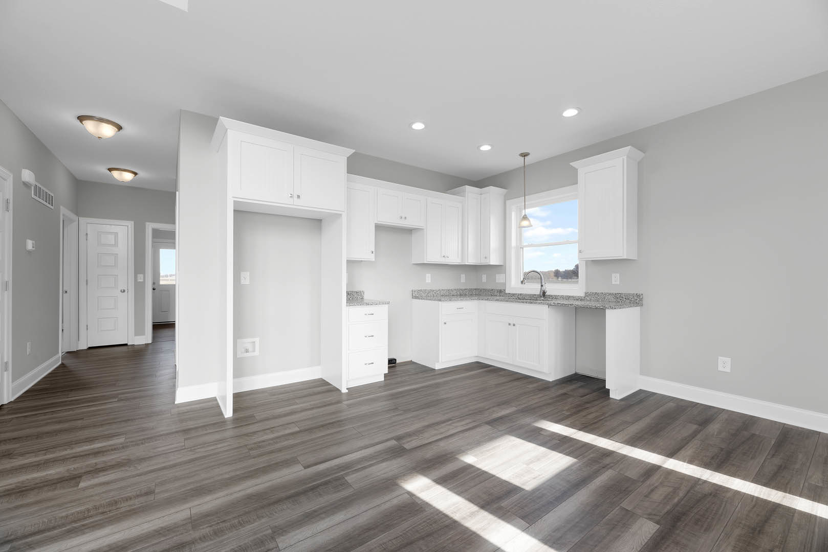 White kitchen with shaker cabinets, stainless hardware, wood flooring, recessed lighting, and a white door with glass window.