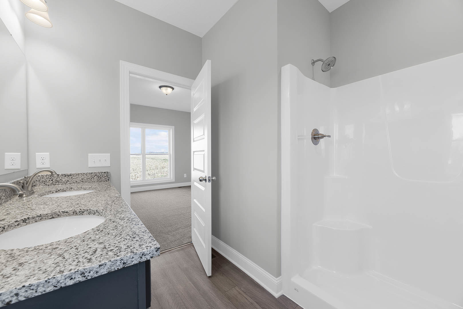 Bathroom with white tile shower, silver faucet, granite countertop sink, wall mirror, and white outlet with two switches on plaster wall