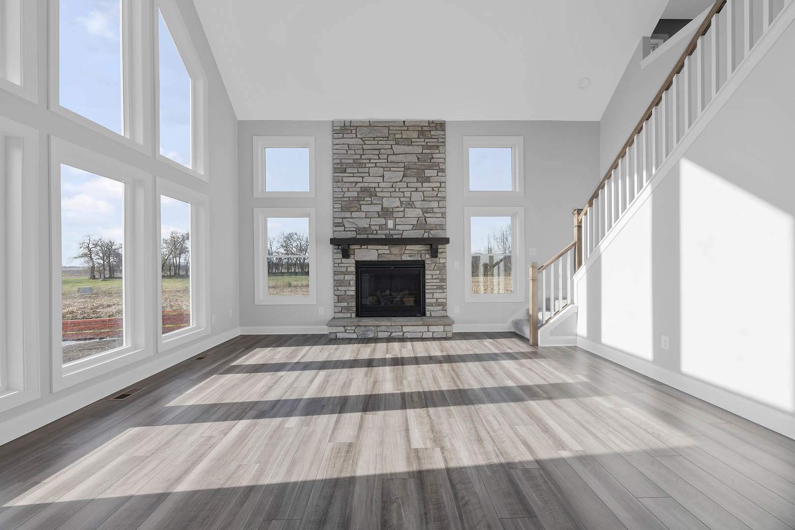 Living room with wood flooring, modern fireplace featuring a glass window and black mantel, staircase with white railing, large windows allowing daylight, white walls with crown