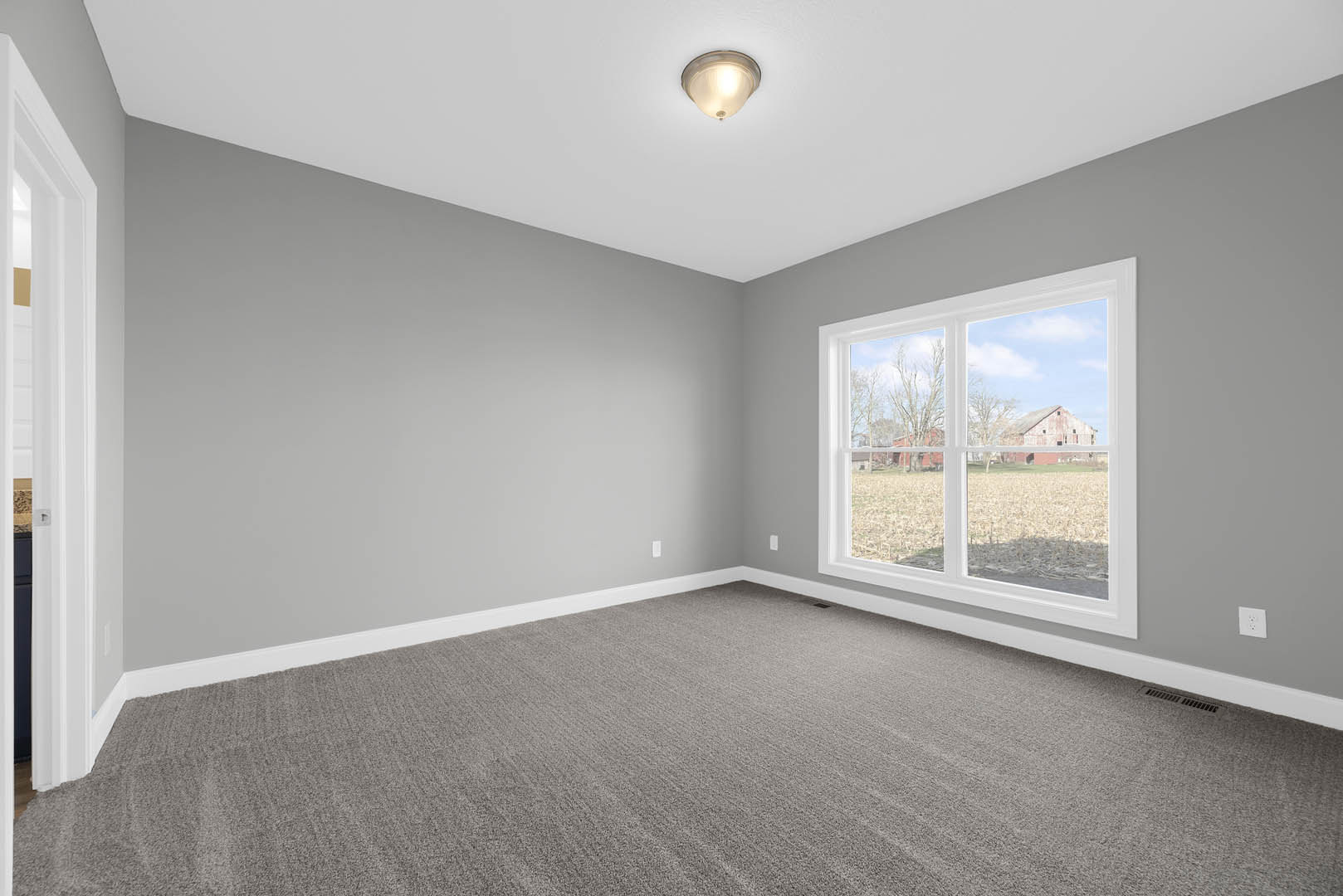 Carpeted room with white trim, large window overlooking a farm and barn, ceiling-mounted light fixture
