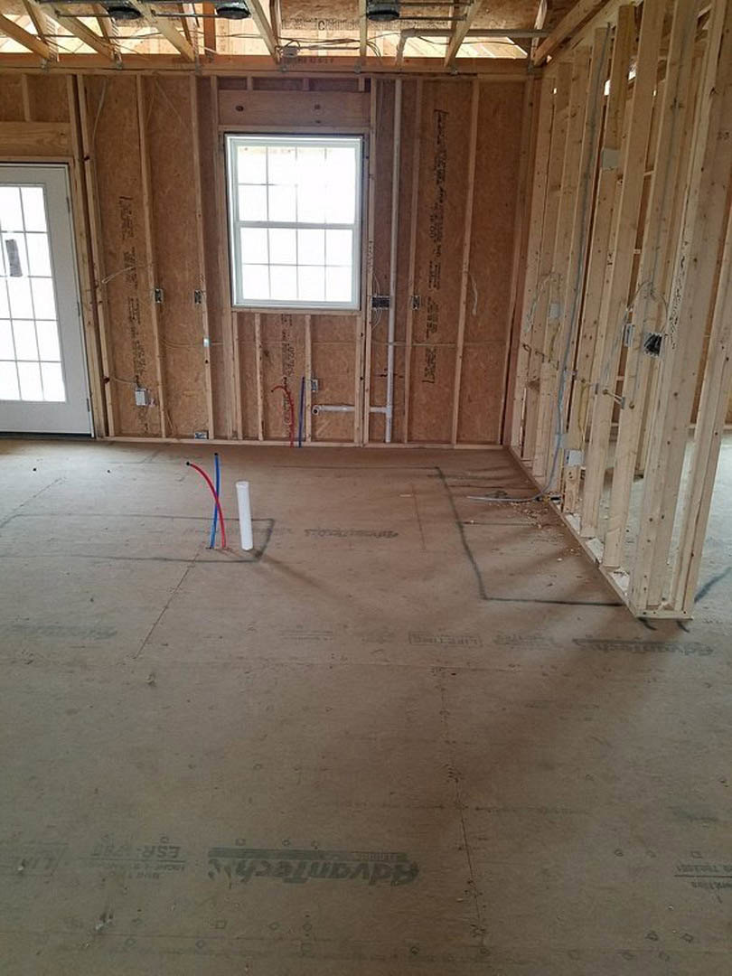 Unfinished room with exposed wood wall, white-framed window, white tile sill, visible red and blue electrical wires, and floor with embedded pipes and wiring