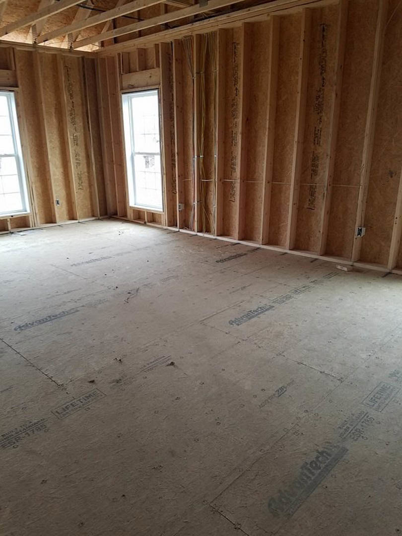 Room featuring wood plank walls, exposed wood beams, large window with wooden frame, and concrete flooring