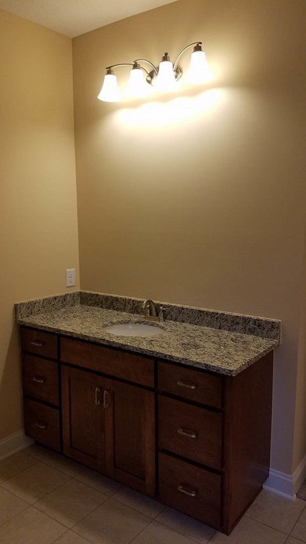 Marble countertop with undermount sink and chrome faucet, three-bulb light fixture above, tile flooring, and cabinetry with visible drawer.