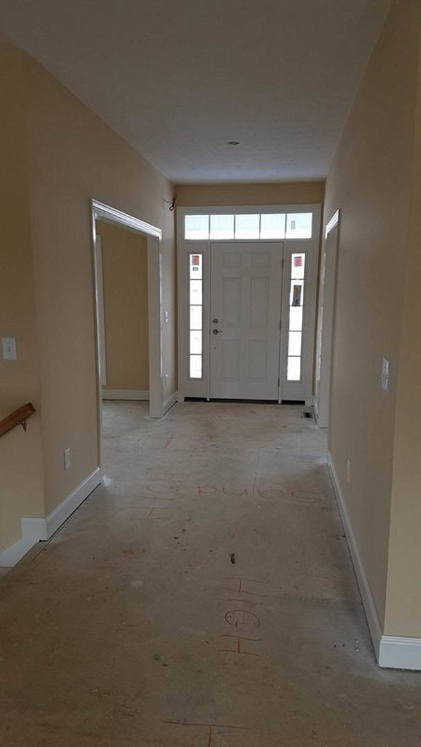 Hallway with light-colored flooring, white walls, a white door with a silver handle, and a glass door; subtle writing visible on the floor
