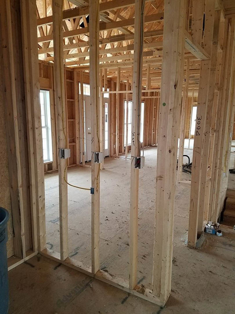 Wood framing and exposed beams in a partially constructed room, unfinished walls with visible insulation, open window with white trim, construction materials scattered on subfloor.