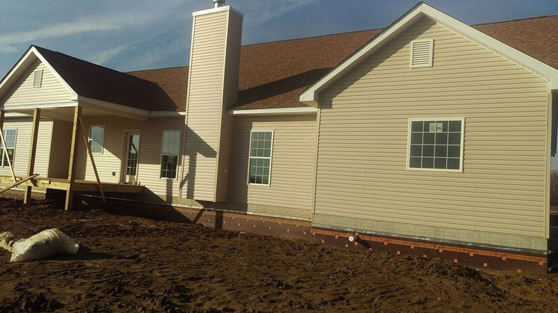 Tan siding house with chimney, square-paned windows, dirt yard with scattered metal studs, large white object resting on ground