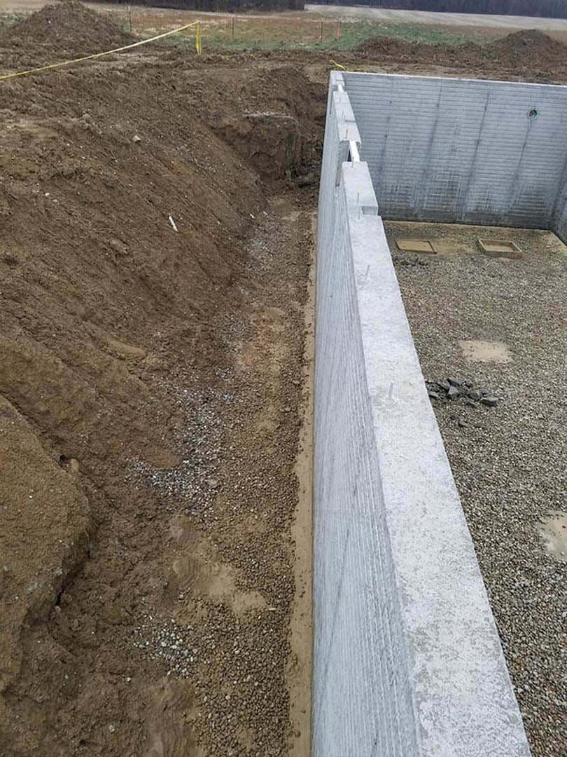 Concrete retaining wall bordering a dirt hill with scattered rocks and visible ground cracks