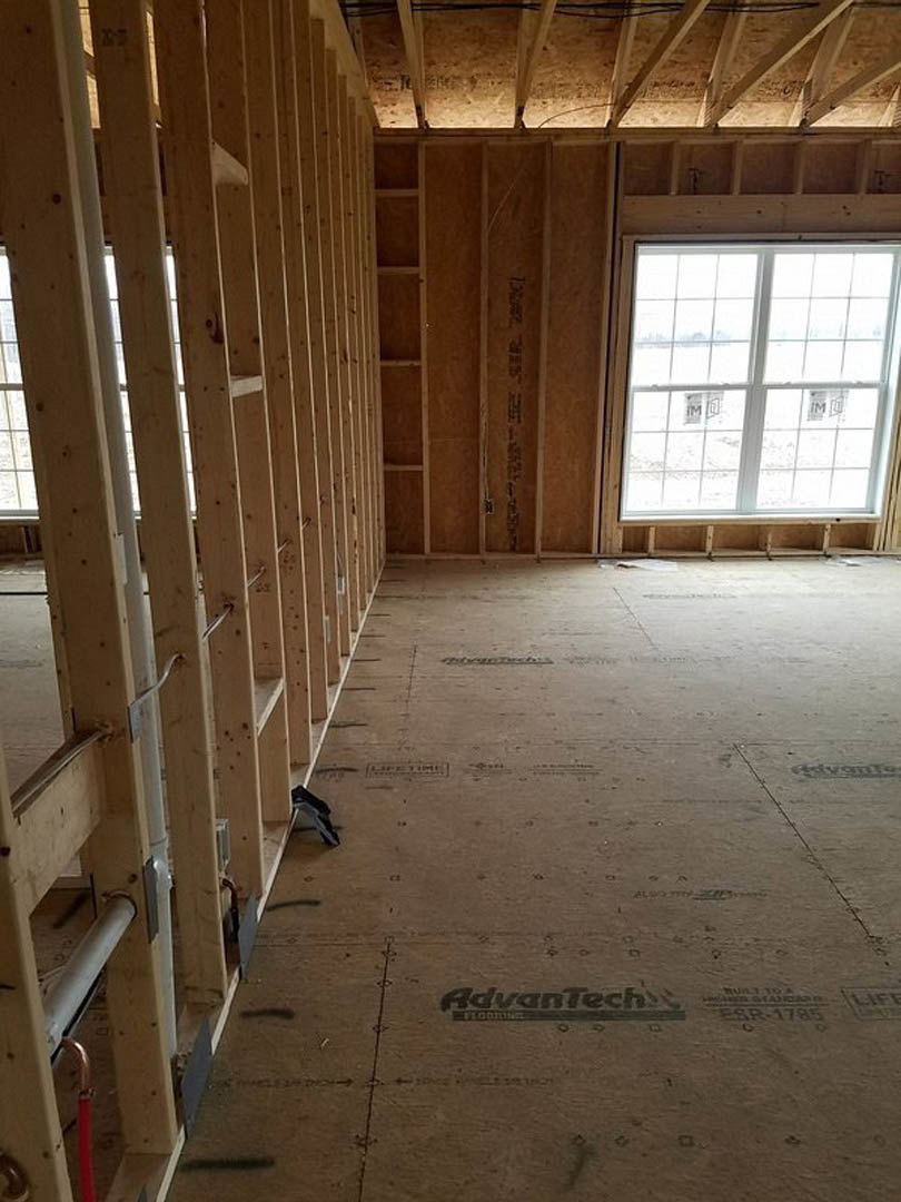 Wood-framed room with exposed beams, unfinished plank walls, large window, and brown surfaces marked with black lettering