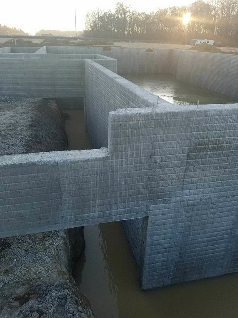 Modern concrete home exterior featuring a central reflecting pool, surrounded by trees and natural landscaping under a bright sky