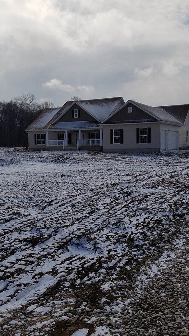 Two-story home with white siding and dark roof, snow covering ground and roof, leafless tree in front yard, cloudy winter sky overhead, white front door and multiple windows