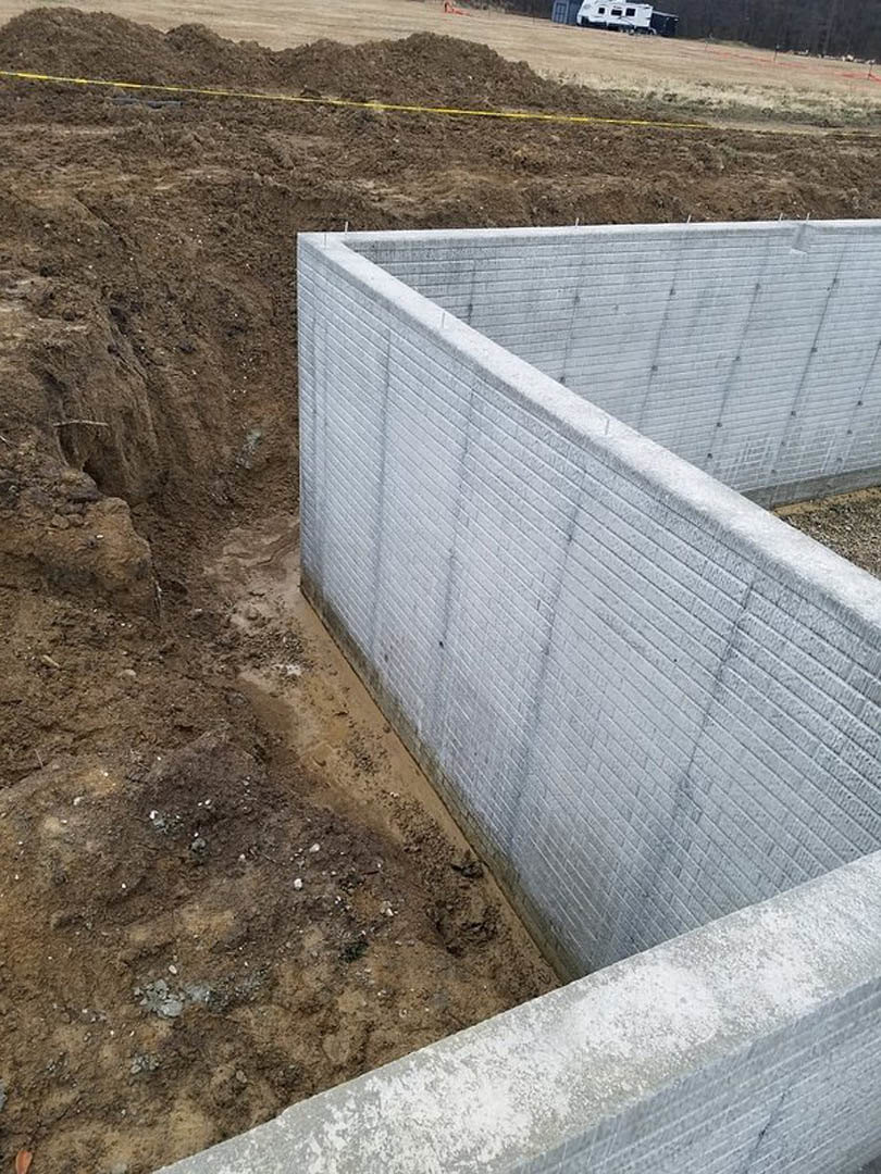 Concrete wall set in a dirt excavation pit with exposed soil and rough ground surfaces