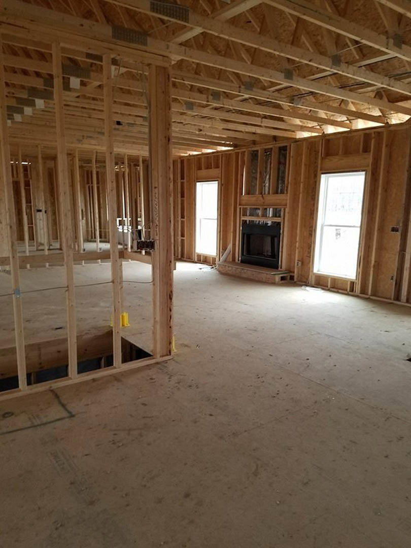 Living room with exposed wood beam ceiling, stone fireplace, hardwood floors, and large windows with white trim