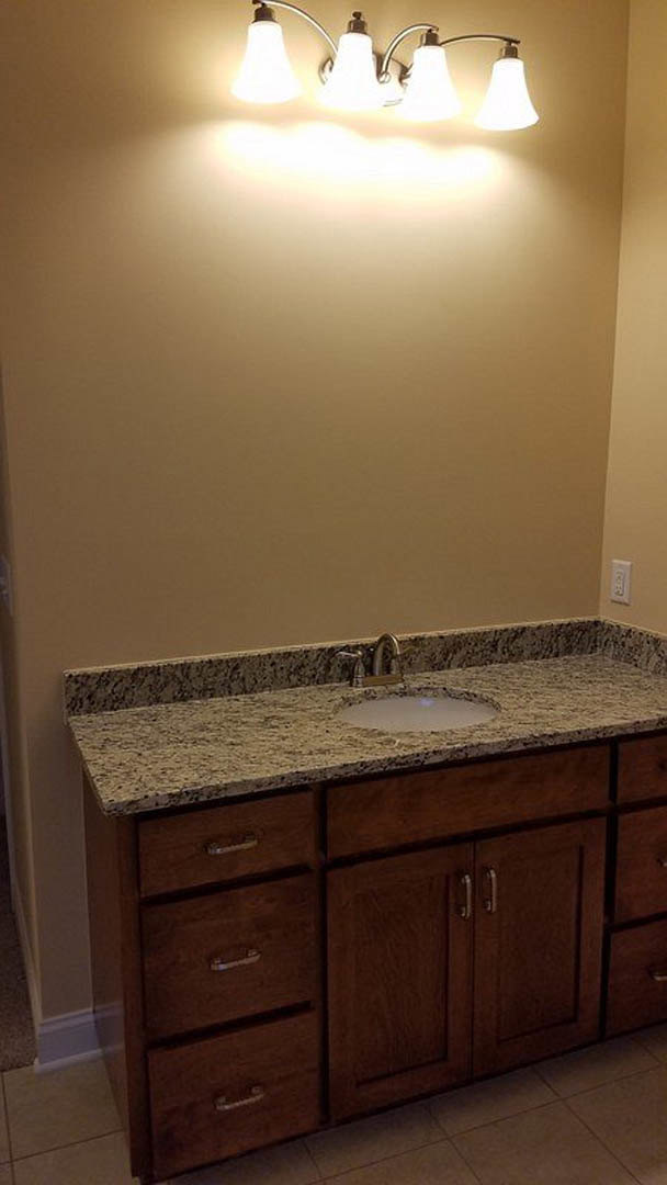 Marble bathroom countertop with undermount sink and chrome faucet, three-light fixture above, brown tile flooring, white cabinetry with drawers and cupboards