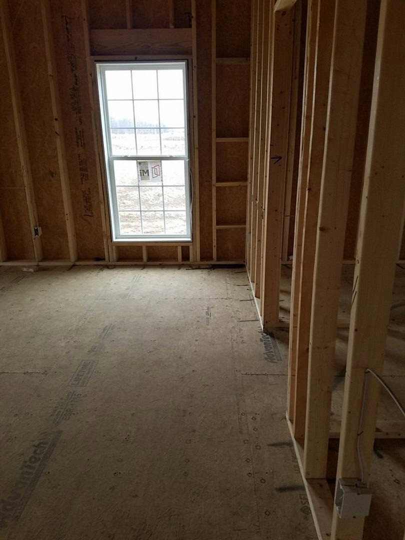 Room under construction with exposed wood framing, window with temporary sign, unfinished walls, and visible lumber beams