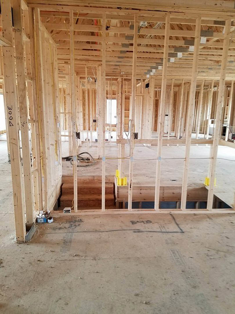 Wood framing and beams with white window frame, concrete floor marked in black, exposed insulation and unfinished ceiling in new home construction.