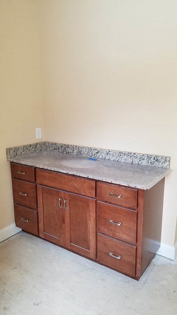 Marble bathroom countertop with wooden drawers and cabinetry, white tile backsplash, and undermount sink