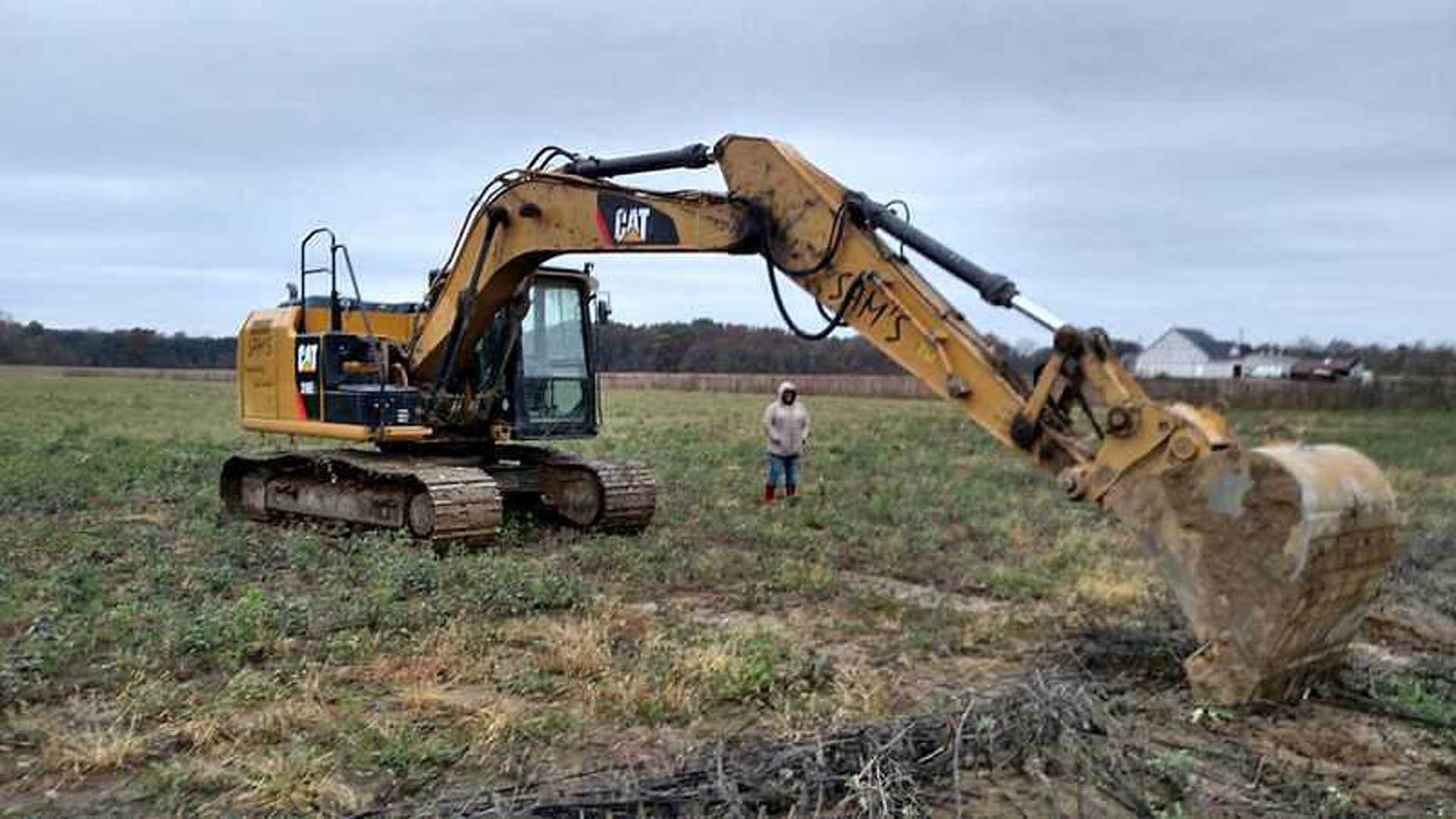Yellow bulldozer parked on grassy field with blue sky overhead, soil and construction equipment visible