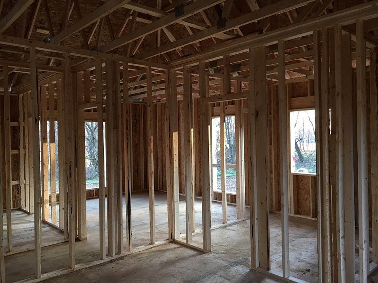 Unfinished room with exposed wood framing, ceiling beams, and large window showing blurred trees outside