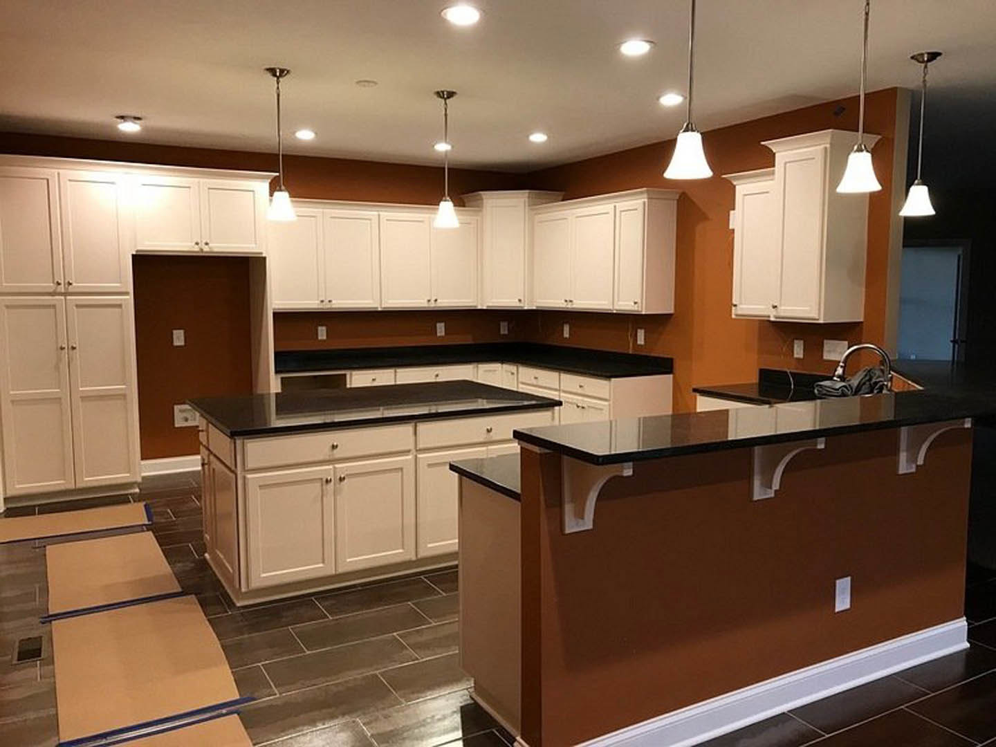 White kitchen cabinets with black countertops, stainless steel sink, tile flooring, ceiling light fixture, and a window above the counter.