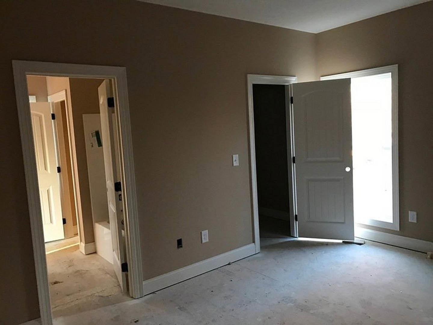 White paneled doors with round handles open to a hallway, light streaming through, reflecting on hardwood floors and a wall mirror.