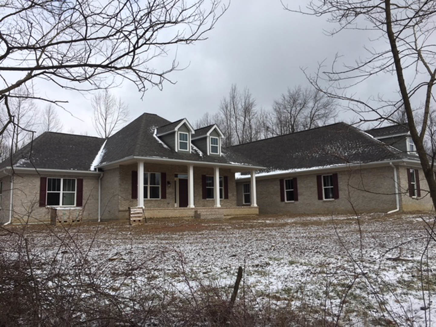 Two-story house with white-framed windows and covered porch, surrounded by snow-covered yard and bare trees under a winter sky