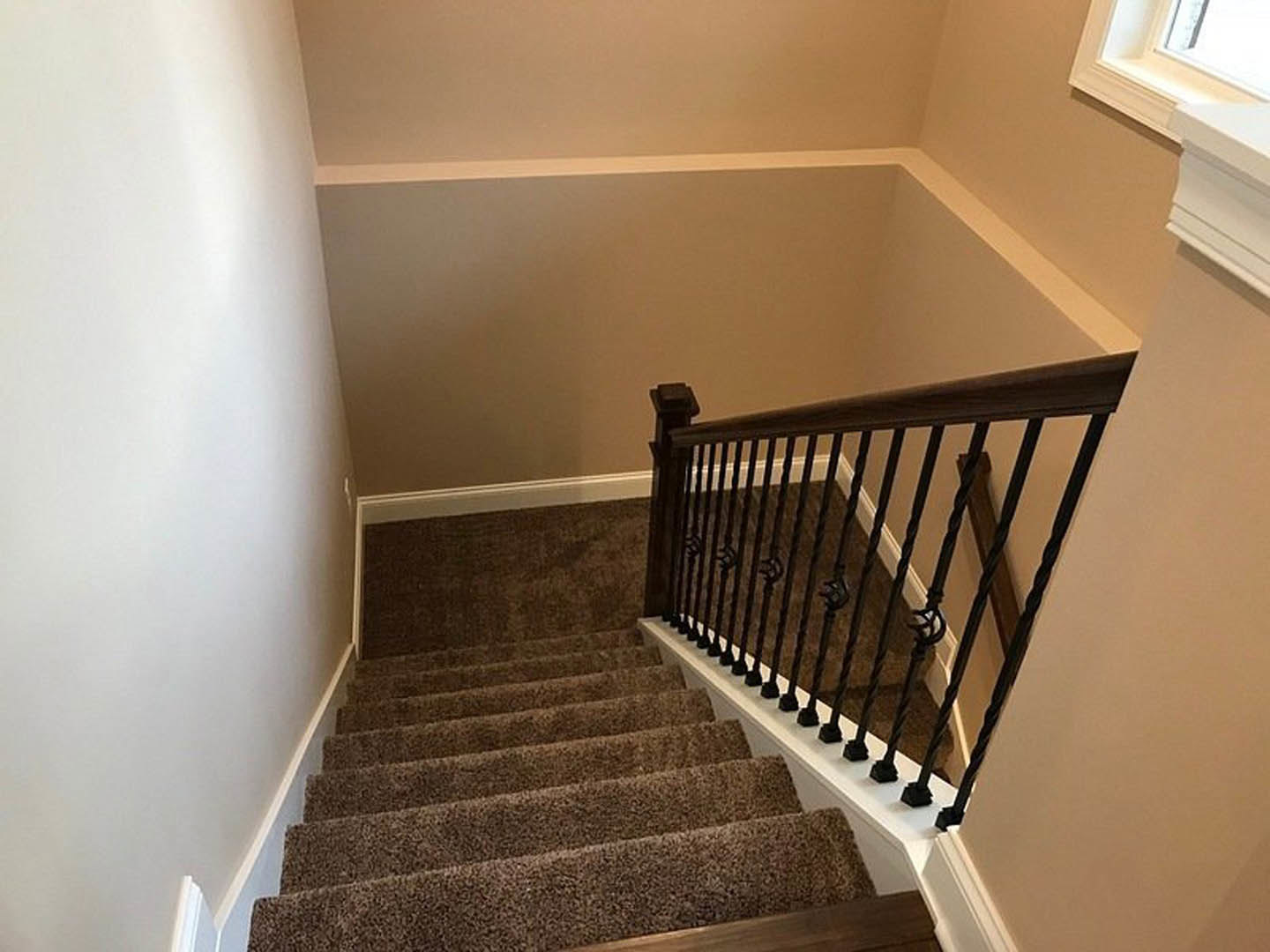 Carpeted staircase with black metal railing, white walls, and decorative molding in a modern home interior