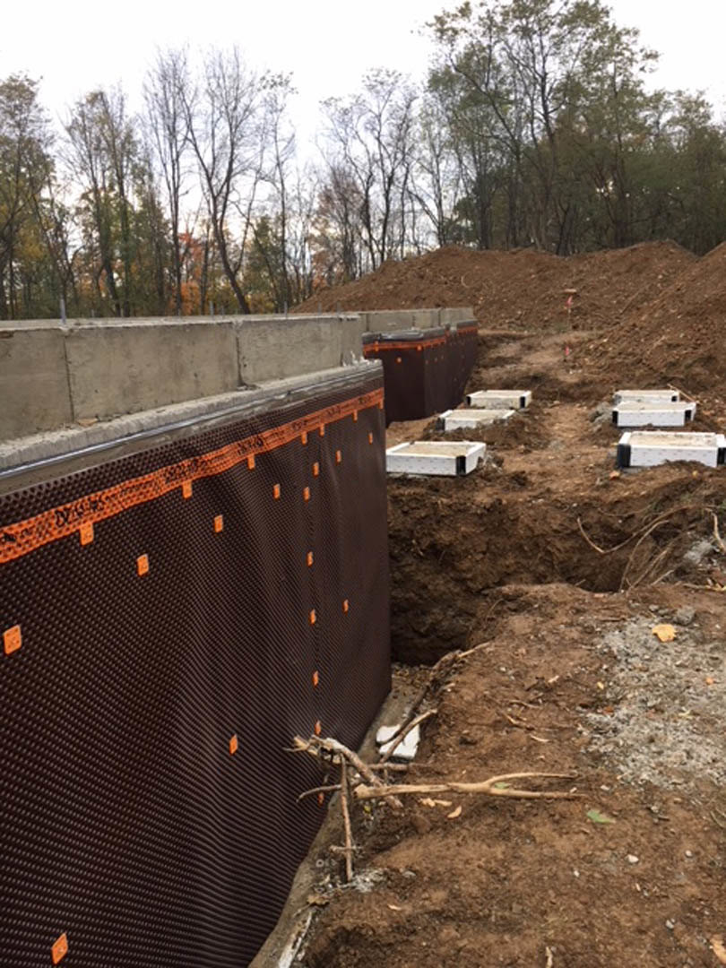 Construction site with exposed foundation, large dirt pile, and surrounding trees under open sky