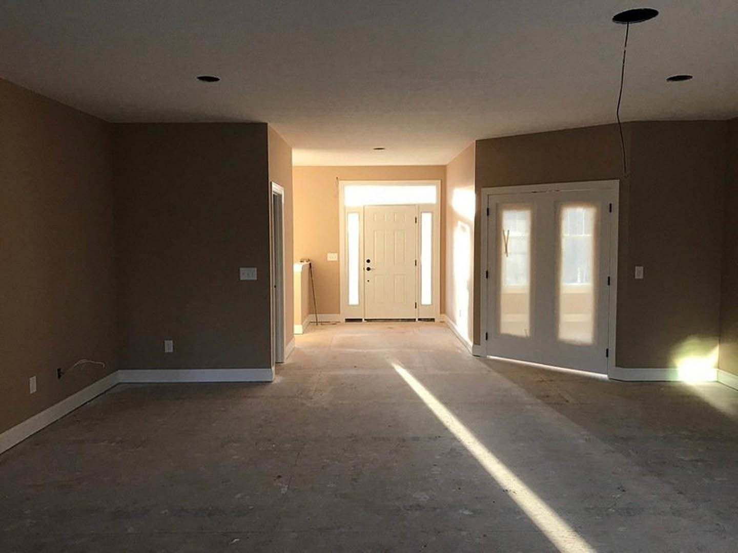 White paneled door with black hardware in a hallway, light reflecting on hardwood floor, smooth plaster walls, and ceiling fixture visible