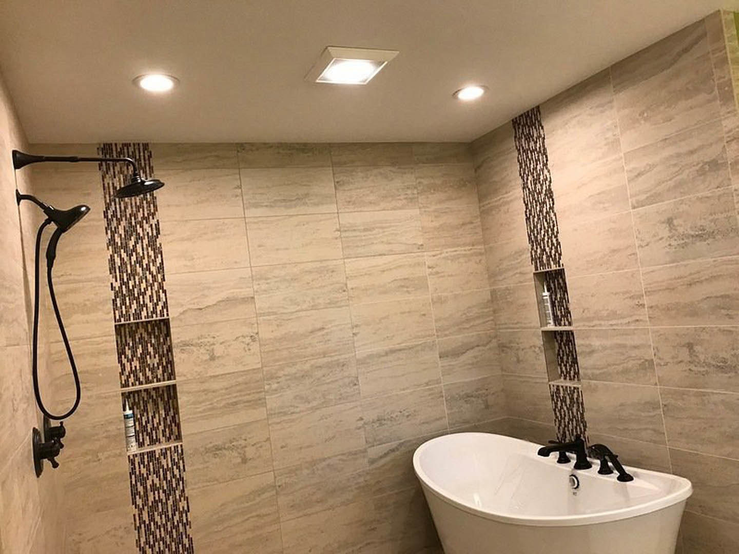 Modern bathroom featuring a freestanding bathtub, glass-enclosed shower, wall-mounted sink with chrome faucet, large mirror, tiled walls, and recessed ceiling light.