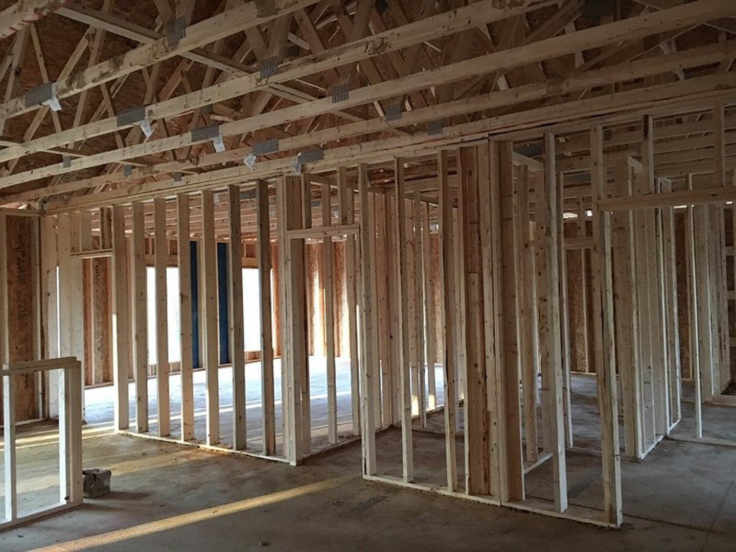 Exposed wooden beams and steel supports inside a partially constructed home, with white pillar and unfinished ceiling and floor visible